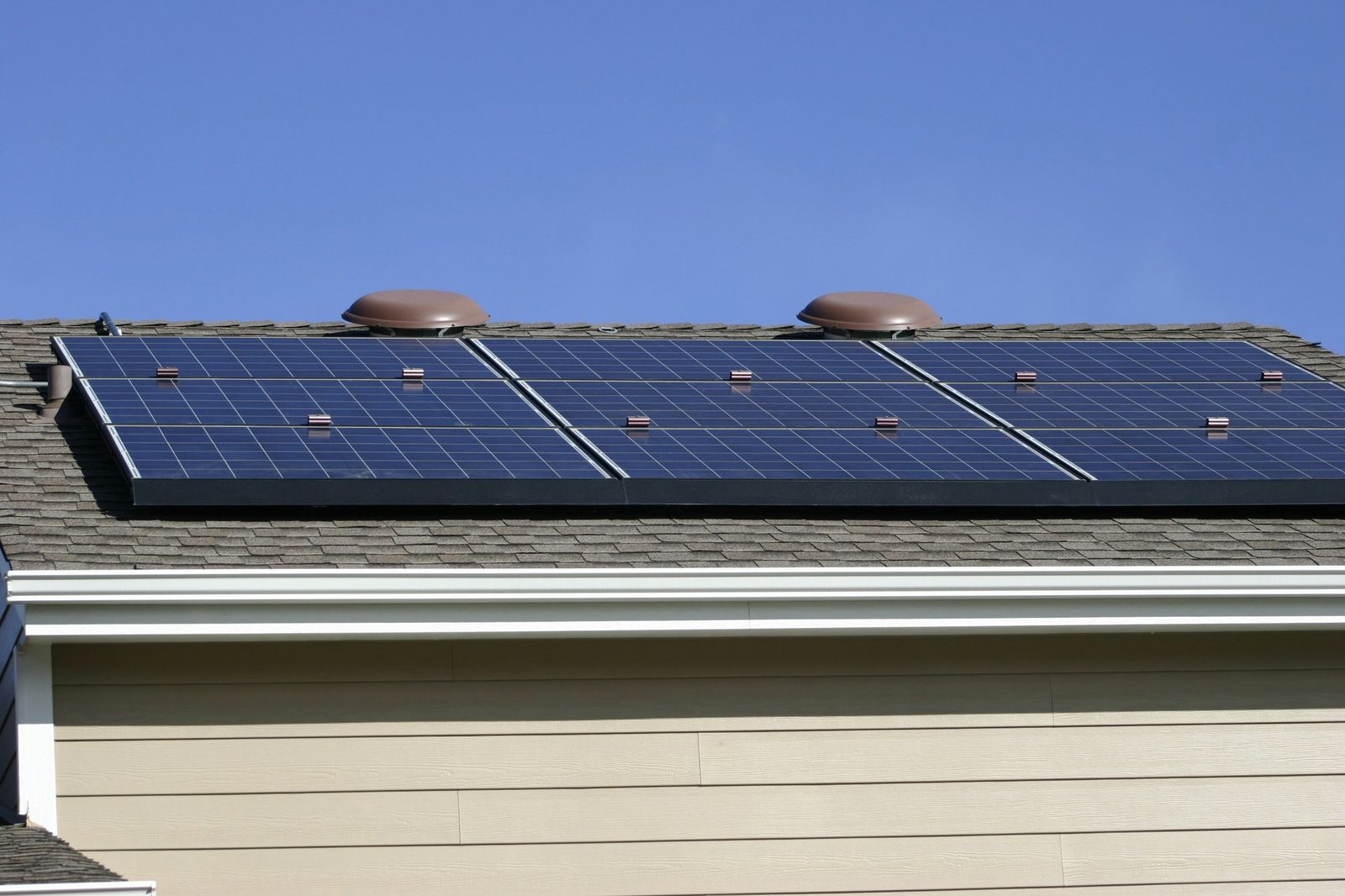 Solar panels on an asphalt shingle roof above beige siding